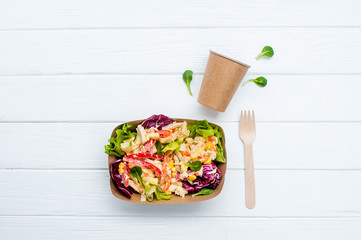 Vegetable salad in the brown kraft paper food container on wooden background