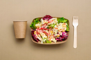 Vegetable salad in the brown kraft paper food container with cup and fork