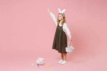 Little pretty blonde kid girl 11-12 years old in light spring dress hold fluffy white bunny rabbit, wicker basket with eggs isolated on pastel pink background. Childhood lifestyle Happy Easter concept