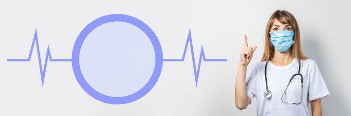 Fototapeta premium Young woman in medical mask and stethoscope pointing her finger on a light background. Added pulse and circle icons. Banner. Doctor concept, high level medical level, vaccination, visit to the doctor