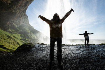 People's dark silhouettes posing against Seljalandfoss waterfall (with lens flares)