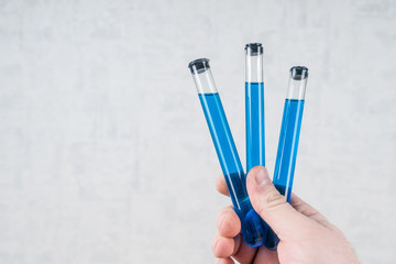 Three test tubes with blue liquid in hand on a white background. Coronavirus, China, antidote, medicine. virus