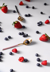 Naklejka na ściany i meble Blueberries, raspberries and strawberries with pink and black spoons with gold on a bluish background. Top view