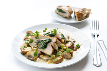 chicken breast fillet stuffed with spinach, served with mushrooms, parsley garnish and a creamy gorgonzola sauce on a plate, white background