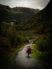 A person with a red raincoat walking along a road during heavy rain in the mountains.