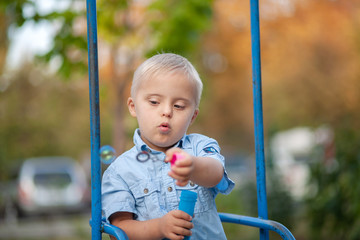 A child with Down cider plays in nature. Toddler blowing soap bubbles. Genetic abnormality in a boy.