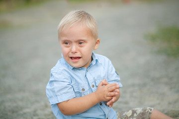 The daily life of a child with disabilities. A boy with Down syndrome sits on the ground and cries....