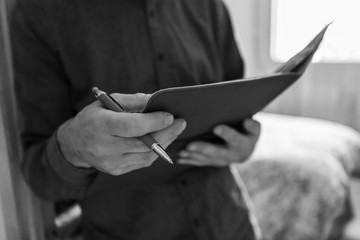 selective focus and close up view of a man's hands as he holds a notebook and pen, he is reading notes, black and white with copy space