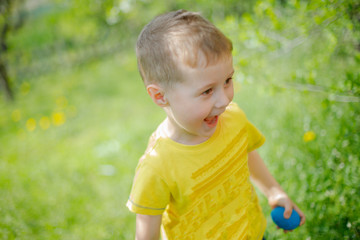 little handsome boy found a blue Eggs. child against green grass. Adorable little boy hunting for easter egg in blooming spring garden on Easter day. holiday and child concept