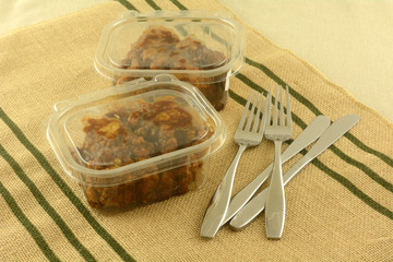 Two take out deli boneless chicken lunches in plastic containers with knives and forks on place mat