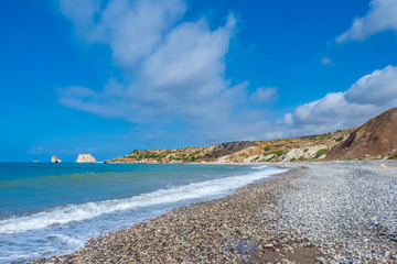 Cyprus. Beach of the island of Cyprus. The rock of Aphrodite in the distance. Beach in Cyprus on the background of blue sky. The shore of the Mediterranean Sea in sunny weather. Mediterranean beaches