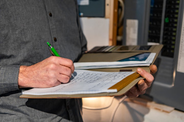 inspector holding a notebook in his hand next to an electric circuit breaker panel, Close up and selective focus of a man taking professional notes.