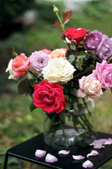 Floral bouquet of different multi colored roses in a glass vase on a dark table with fallen petals. Mother's Day, Valentine's Day, International Women's Day. Spring, summer bouquet