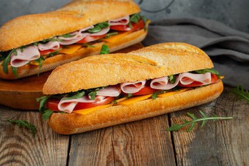 Two Long baguette Sandwiches with arugula, slices of fresh tomatoes, ham and cheese