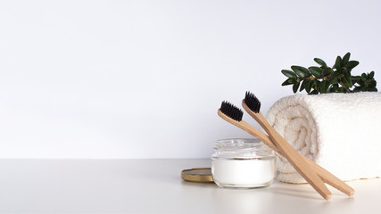 Two bamboo toothbrushes, natural tooth powder, white towel and greenery on light gray table. Zero waste bathroom, eco friendly dental care products and sustainable lifestyle concept. Copy space.