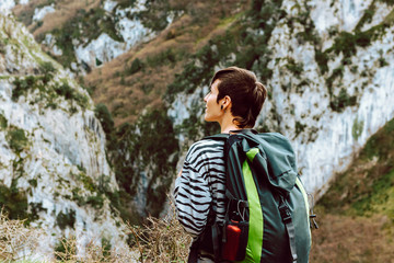 Young hiker with green backpack and red canteen observes the landscape.