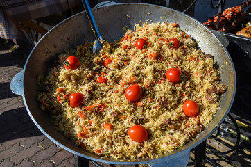 Tasty Uzbek pilaf in a cauldron on fire in the open air at street food festival.