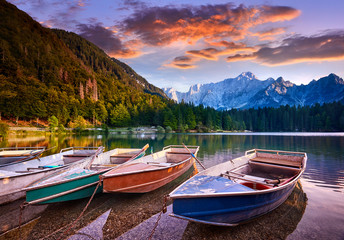 Naklejka na ściany i meble Amazing view on Lago di Fusine Inferiore at sunrise. Splendid morning scene of Julian Alps, Province of Udine, Italy, Europe. Beautiful forests are reflected in the quiet lake. Four pleasure boats