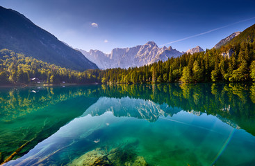 Amazing view on Lago di Fusine Inferiore at sunrise. Splendid morning scene of Julian Alps, Province of Udine, Italy. Beautiful forests are reflected in the quiet lake. Dolomites mountains.