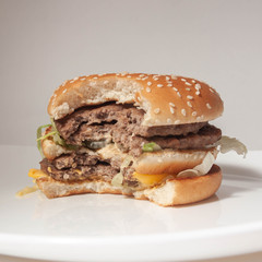 half-eaten Burger with two cutlets on a white plate and a light background, side view