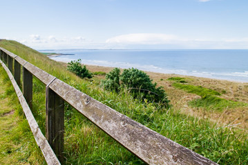 View of the ocean past the sand dunes over a wooden fence