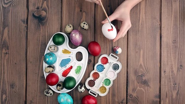 Hand painted Easter eggs, paints and brushes on wooden background. Preparation for the holiday. Girls hands draw a pattern