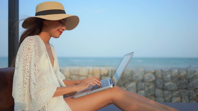 Female traveler or a digital nomad working remotely on a laptop, perhaps writing a blog on the internet while sitting near the ocean during the day.