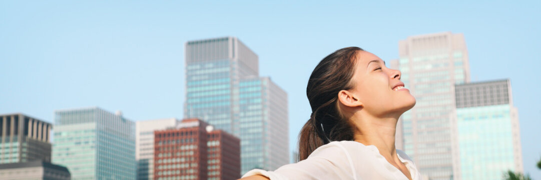 Happy healthy woman taking deep breath in city clean air for pollution concept panoramic lansdcape header banner. Asian lady in Asia face portrait with closed eyes.