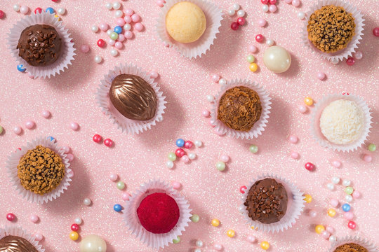 Chocolate, nut and coconut candies on a pink background, decorated with sugar sprinkles of candy, top view