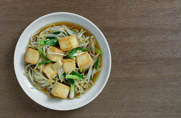 top view of stir fried fish tofu with bean sprout in a ceramic dish on wooden table. asian homemade style food concept.