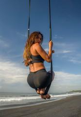 aero yoga beach workout - young attractive and athletic woman practicing aerial yoga exercise training acrobatic  body postures on blue sky over sea in Bali island