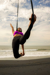 aero yoga beach workout - young attractive and athletic woman practicing aerial yoga exercise training acrobatic  body postures on blue sky over sea in Bali island