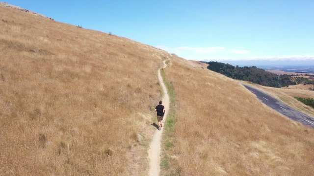 Tracking drone shot of man running on single trail with blue sky in background.
