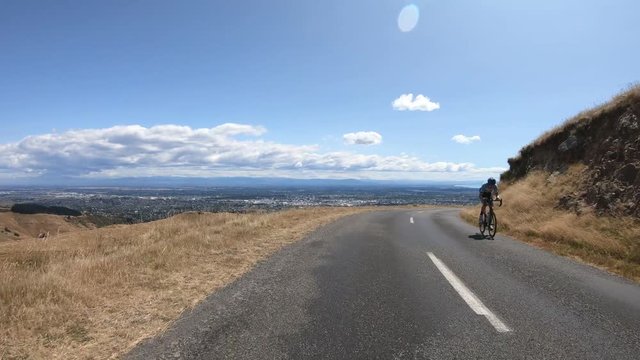 POV from car bonnet driving on hill road with city and clouds in background.