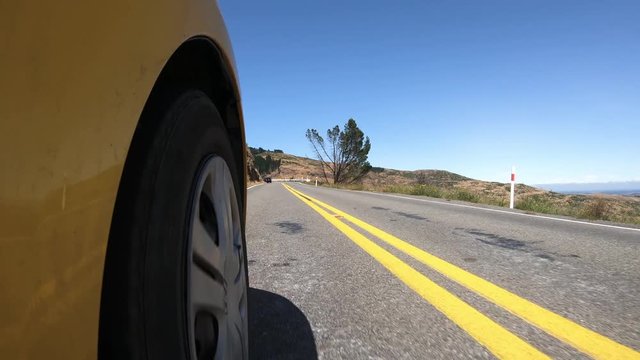 Car front wheel as traveling on mountain road with blue sky and traffic.