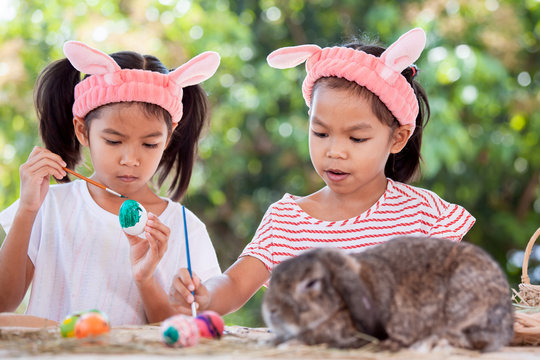 Two cute asian child girls drawing and painting on easter eggs together prepare for easter day. Children and Holland lop rabbit in easter festive.