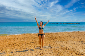 Fototapeta na wymiar A girl in a swimsuit dancing on the beach near the sea in summer.