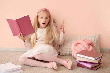 Little girl with raised index finger and book near color wall
