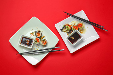 Fototapeta na wymiar Dirty plates with sushi rolls and sauce on color background
