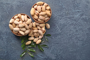 Bowls with tasty pistachio nuts on grey background