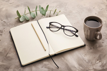 Notebook with cup of coffee, eyeglasses and pencils on grunge background