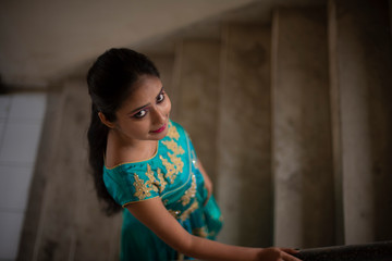 Fototapeta premium Fashion portrait of an young and attractive Indian Bengali brunette girl in Indian traditional dress climbing upstairs. Indian fashion portrait and lifestyle.
