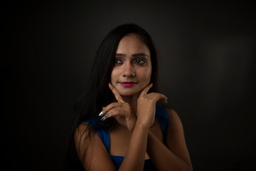 Close up fashion portrait of an young and attractive Indian Bengali brunette girl with blue western dress in front of a black studio background. Indian fashion portrait and lifestyle.