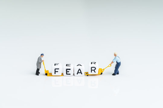 Fear and greed in investment, financial risk or afraid of crisis, miniature people men pulling forklift with block building the word Fear on white background