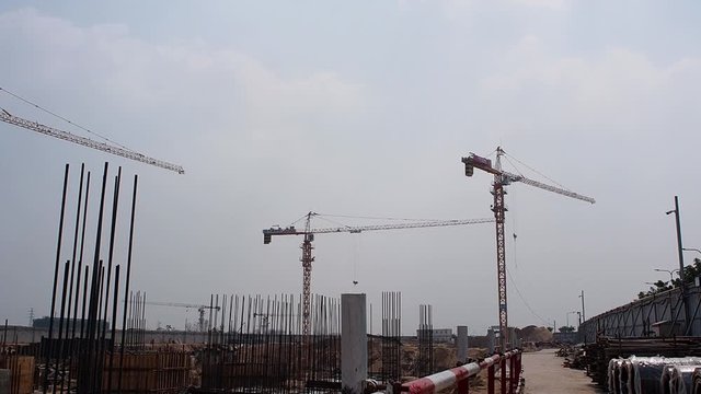 Static wide shot of many industrial cranes working on construction site during daytime