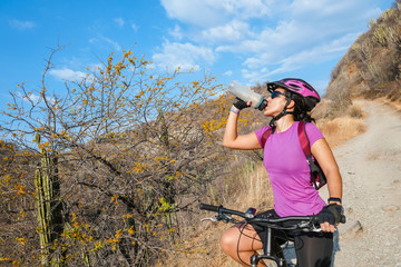 happy woman riding a mountain bike getting hydrated, enjoying a summer day in the mountains Outdoor sports activity, lifestyle concept