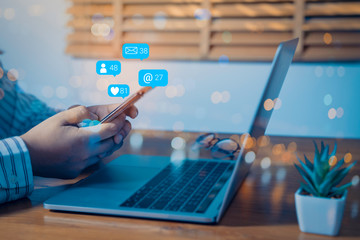 Person using a social media marketing concept on laptop computer with notification icons of like, message, comment and star above laptop keyboard.