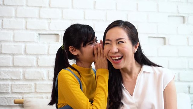 Asian family of teenage girl gossiping at mature woman's ears at home. Fun time with daughter and mother