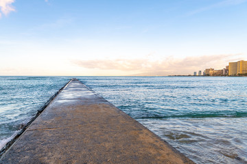 Obraz premium A beautiful stone pier walkway at the ocean at Waikiki Beach in Honolulu, HI, at sunset.