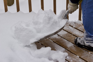 Close up view of an unseen person shoveling deep snow of a wooden deck surface
